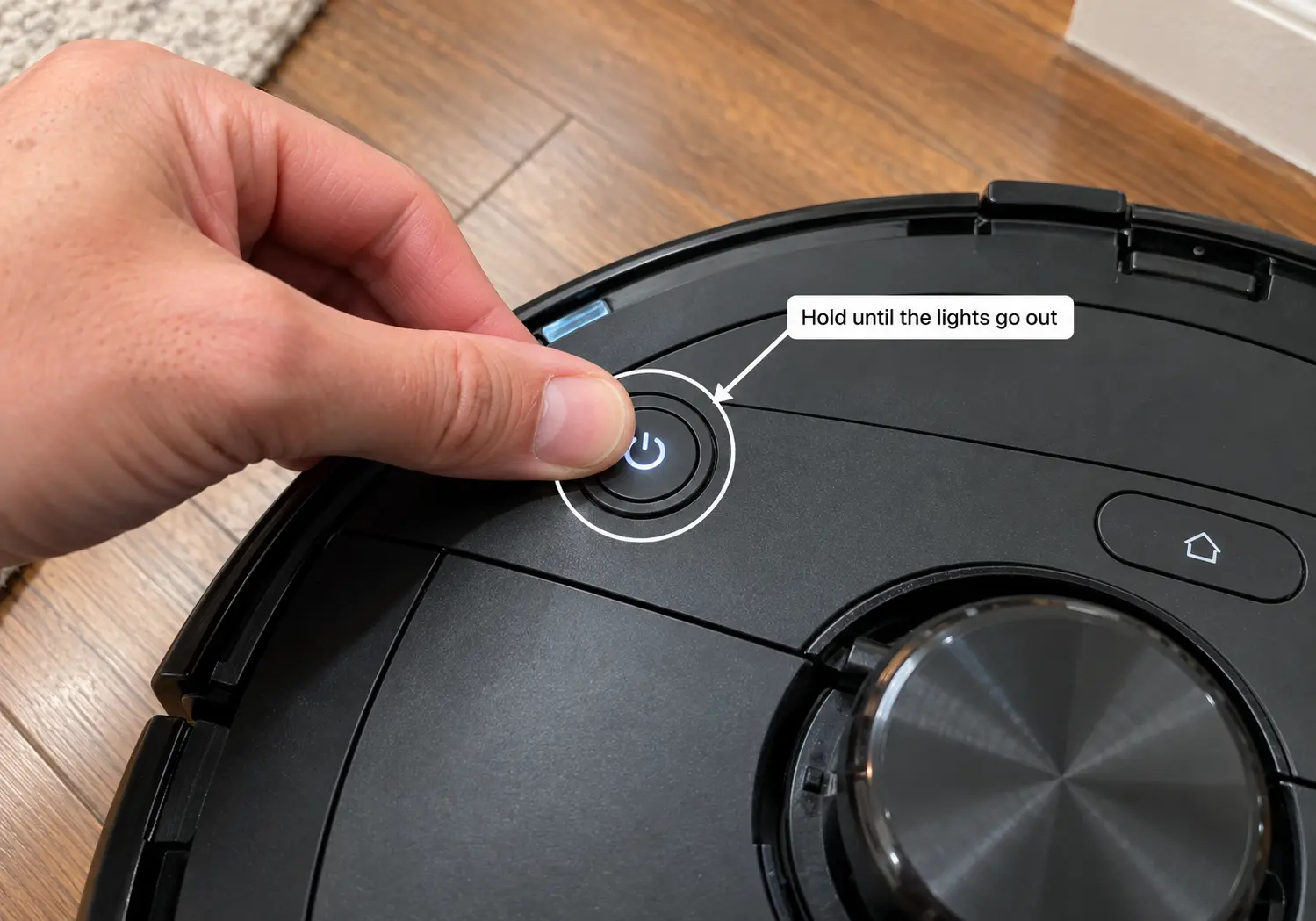 hand holding the power button on a robot vacuum to restart it